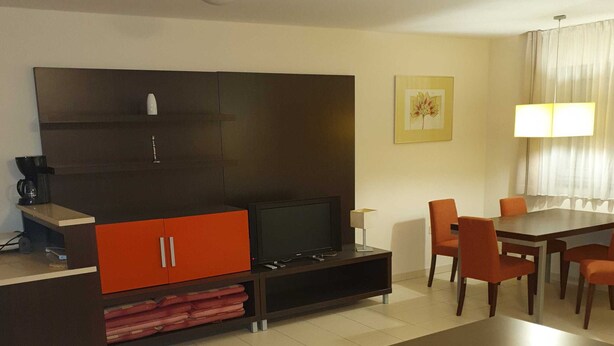 A modern hotel room with a sofa, a coffee table, a TV, a dining table with chairs, and a cabinet.