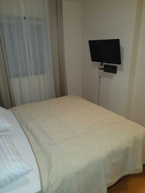 A hotel room with a bed, a TV mounted on the wall, and a window with sheer curtains. - Marina Portorož Family Friendly Apartment 5 (Piran)