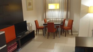 A living room with a TV, sofa, and dining table with chairs.