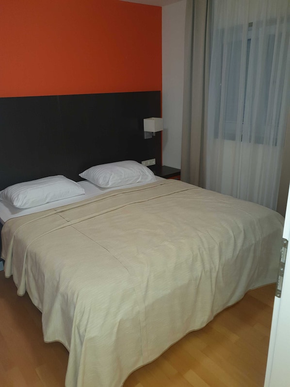 A hotel room with a bed, a nightstand, a lamp, and a window with curtains. - Marina Portorož Family Friendly Apartment 5 (Piran)