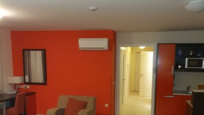 A compact hotel room with a bed, a sofa, a small table, a desk, and a kitchenette.