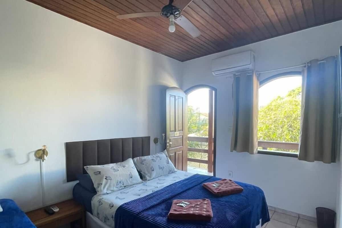 Ein Schlafzimmer mit Bett, Nachttisch, Deckenventilator, Fenster mit Vorhängen und einer zur Außenseite führenden Tür.