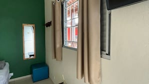 A room with a green wall, a window with beige curtains, a wooden table with a remote control, and a blue bench. - Chill Inn Pousada Paraty (Paraty)