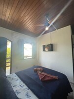 Een slaapkamer met een bed, een plafondventilator, een raam en een aan de muur bevestigde televisie.