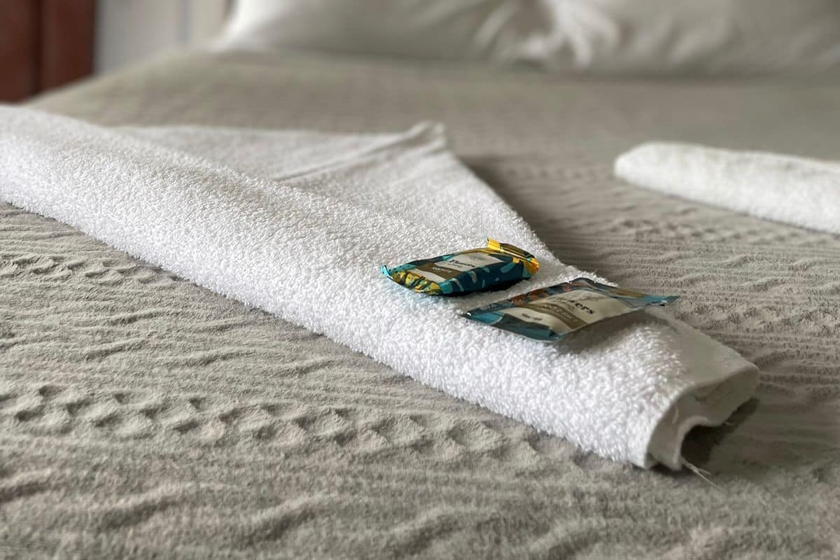 Ein ordentlich bezogenes Bett mit weißer Decke und Kissen, ein aufgerolltes Handtuch und eine Zeitschrift auf dem Bett.