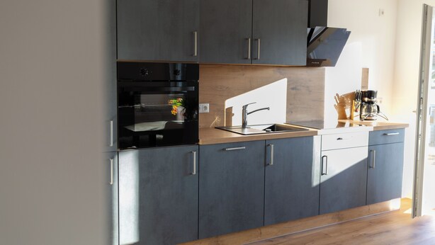 A modern kitchen with dark cabinets, a built-in oven, and a coffee machine.