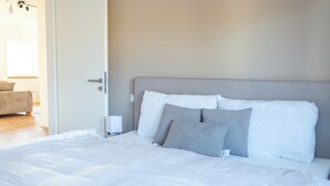 A neatly made bed with white and grey bedding, a bedside lamp, and a door leading to another room.