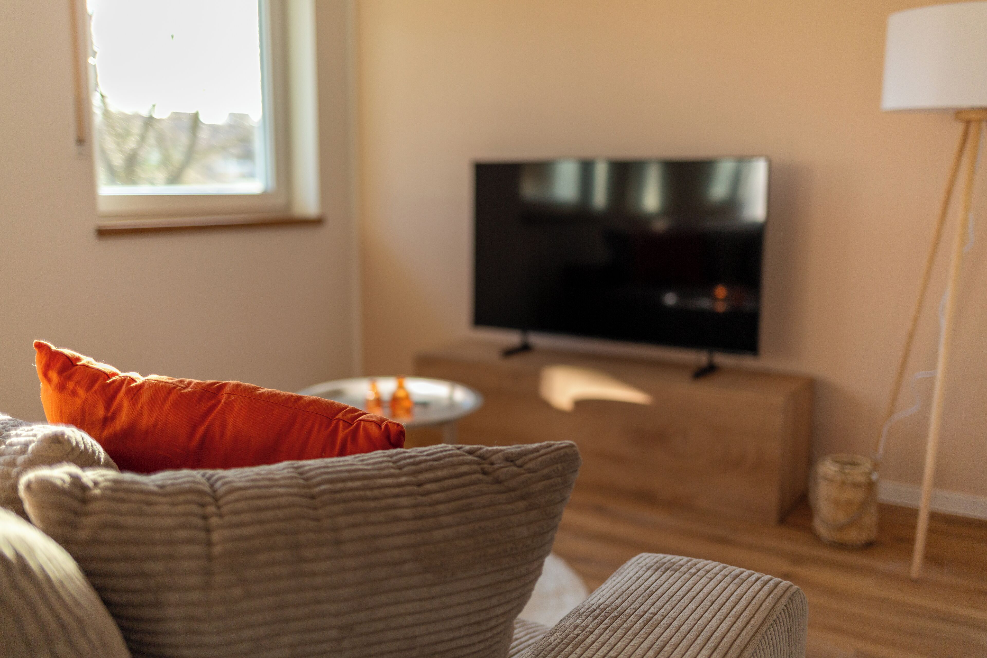 A living room with a television on a stand, a sofa with cushions, a small table, and a floor lamp.