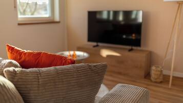 A living room with a television on a stand, a sofa with cushions, a small table, and a floor lamp.