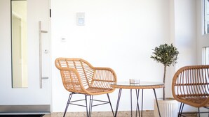 A room with two wicker chairs and a small table, a potted plant, and a door with a handle.