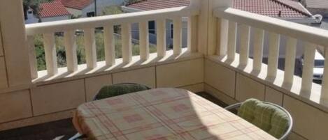 A balcony with a table and chairs, overlooking a coastal area with houses and the sea.