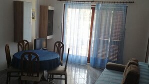 Ein Zimmer mit Esstisch, Stühlen, einer Couch, einem Fernseher und einem Fenster mit Vorhängen.