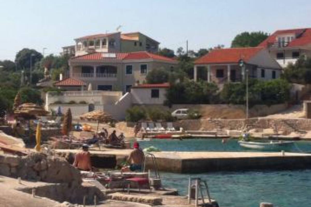 A coastal building with a red roof, situated near a marina with boats and a swimming area.