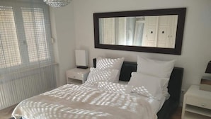 A bedroom with a large bed, a nightstand, a dresser, a mirror, and a window with blinds.
