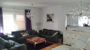 A modern living room with a sofa set, a wooden coffee table, a white chair, and a chandelier.