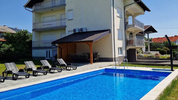 A two-story building with a swimming pool, outdoor seating, and a covered patio area.