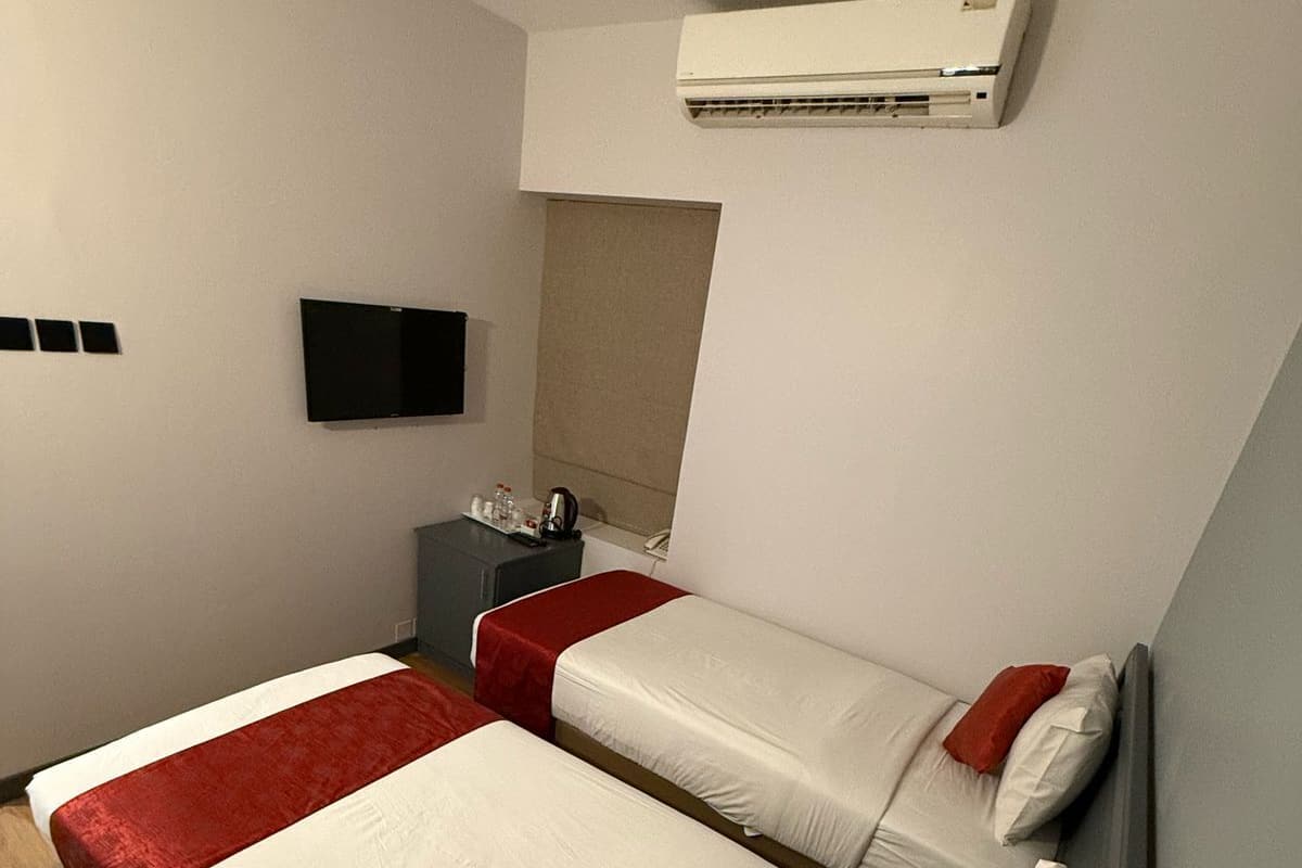A hotel room with two beds, a TV, and an air conditioning unit.
