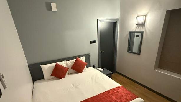 A modern hotel room with a large bed, a bedside table, a nightstand, a wall-mounted light, and a door. - AL SHARQ HOTEL L L C (Sharjah)