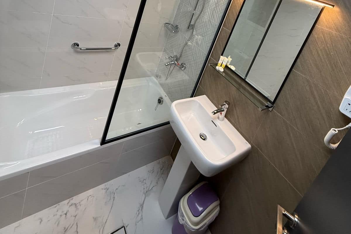 A modern bathroom with a glass-enclosed shower, a white sink, and a mirror with integrated lighting.