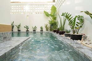 Una piscina con borde de azulejos, rodeada de diferentes macetas con plantas.