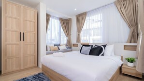 Un dormitorio moderno con una cama grande, un armario de madera y vistas de la ciudad a través de cortinas translúcidas.