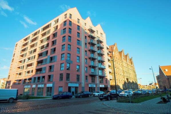 Un edificio de varios pisos con balcones, estacionamiento y cielo despejado.