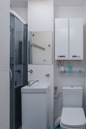 A compact bathroom with a glass shower enclosure, a white toilet, and a small sink with a mirror above it. - XO Luxury Metro Residence (Warszawa)