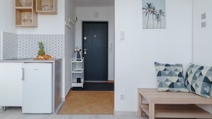 Eine kleine Küche mit einem Kühlschrank, einem Holzregal mit Gläsern, einer sechseckig gefliesten Spritzschutzwand und einer Tür zu einem Flur.