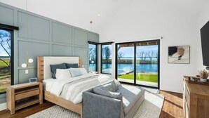 Un dormitorio moderno con una cama grande, mesitas de noche, un escritorio y vistas a un lago.