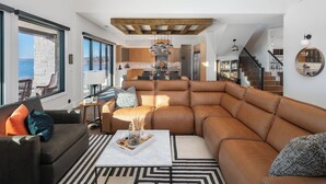 Una sala moderna con un amplio sofá de cuero, una mesa de centro con objetos decorativos, y vistas al área de cocina y comedor.
