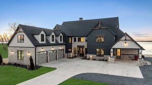 Una casa grande y moderna con fachada de piedra, varios portones de garaje y un césped bien cuidado.