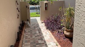Un étroit sentier, pavé de carreaux décoratifs, mène à une entrée fermée par un portail.