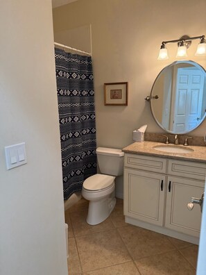 Baño con inodoro, lavabo, espejo y cortina de ducha estampada.