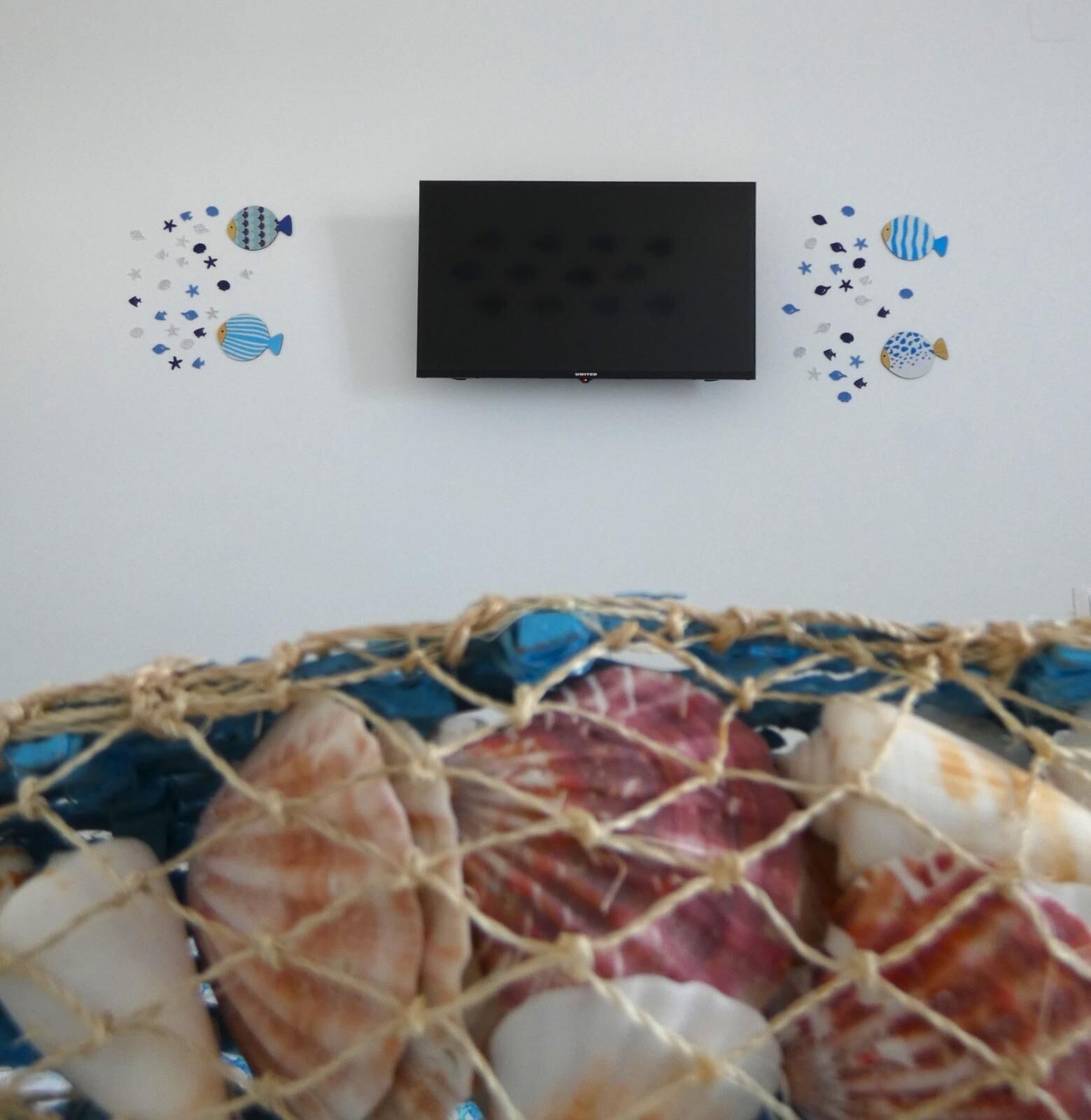 Un televisor montado en la pared con una cesta de conchas marinas debajo.
