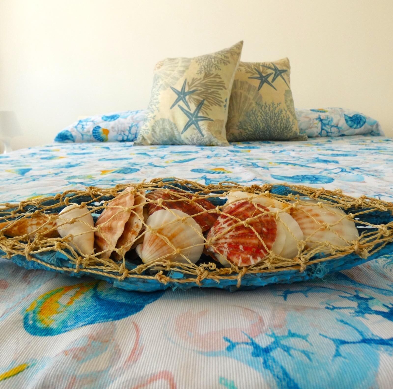 Ein Bett mit blauer Blumenbettwäsche, einem Netz voller Muscheln und zwei Sternen-Kissen.