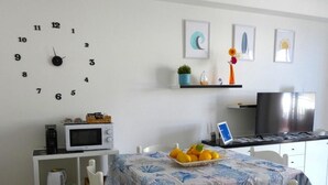 Un espace repas comprenant une table, des chaises, une horloge, un four à micro-ondes, une bouilloire, un grille-pain, un ordinateur portable et un téléviseur.