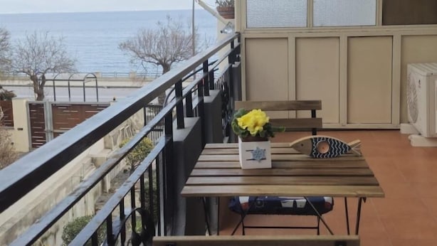 Un balcon avec vue sur la mer, une table en bois, une chaise et une petite plante.