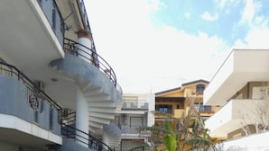 Un chemin bordé de verdure et de bâtiments modernes dotés de balcons, sous un ciel dégagé.