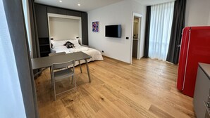 Ein modernes Hotelzimmer mit einem Bett, einem Fernseher, einem Esstisch und einem roten Kühlschrank.