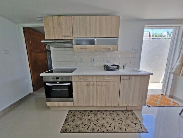A kitchen with light wood cabinets, a built-in oven, and a stainless steel range hood. - Charming studio in quiet, adorable location in Christ Church with WiFi, AC & TV. (Christ Church)