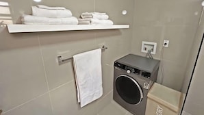 Un baño moderno con pared de azulejos grises, lavadora empotrada, toallero y estante con toallas dobladas.
