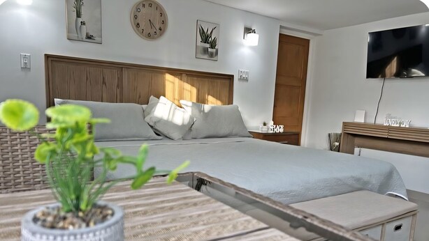 Un dormitorio moderno con una cama grande, una mesita de noche, un televisor y un reloj en la pared.