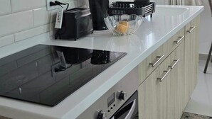 A modern kitchen with light wood cabinets, a white countertop, a built-in stove, and a range hood. - Charming studio in quiet, adorable location in Christ Church with WiFi, AC & TV. (Christ Church)