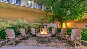 A patio area with a fire pit surrounded by Adirondack chairs and a stone fire table.