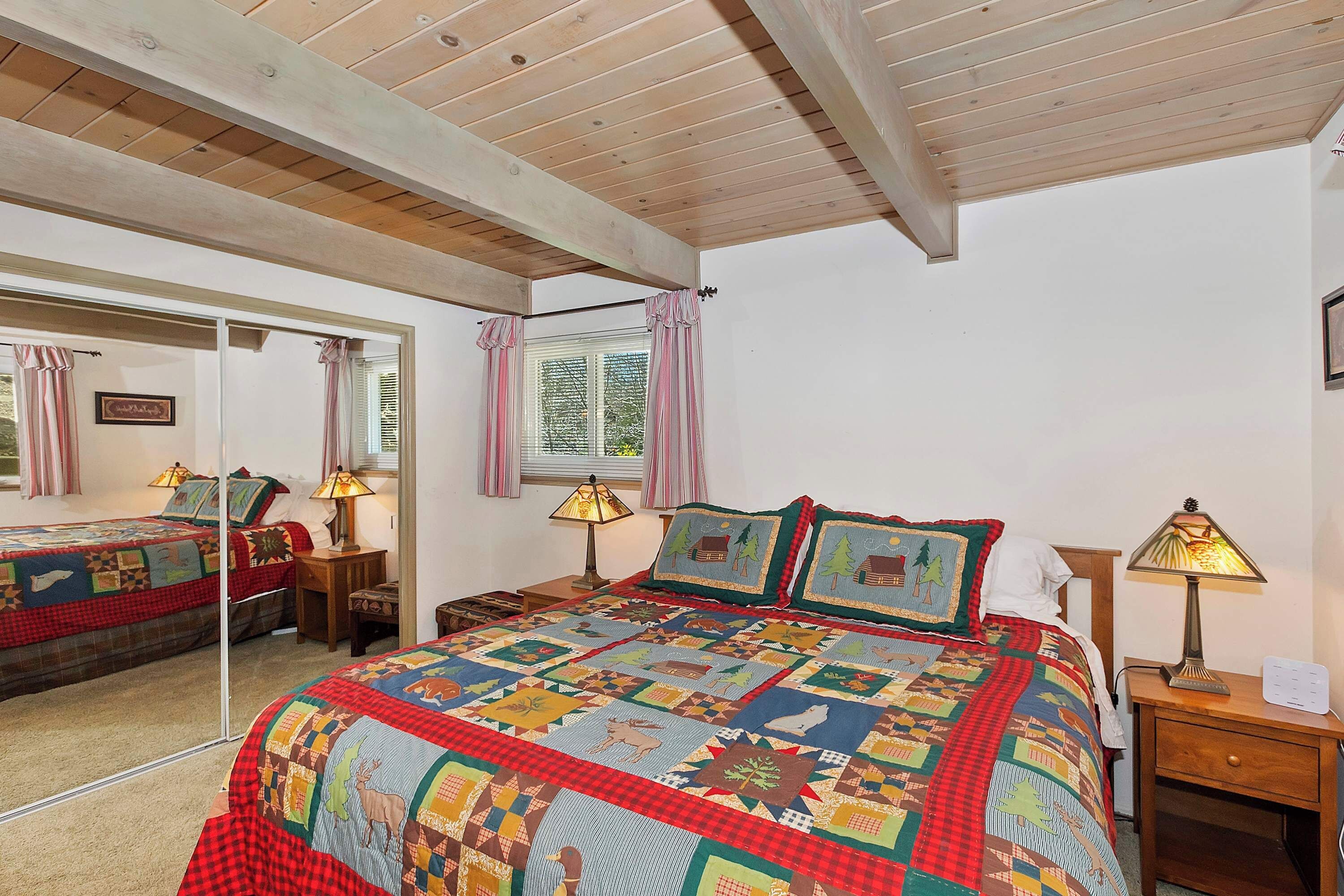 A bedroom with a large bed, a mirror, a window with curtains, and two bedside tables with lamps.