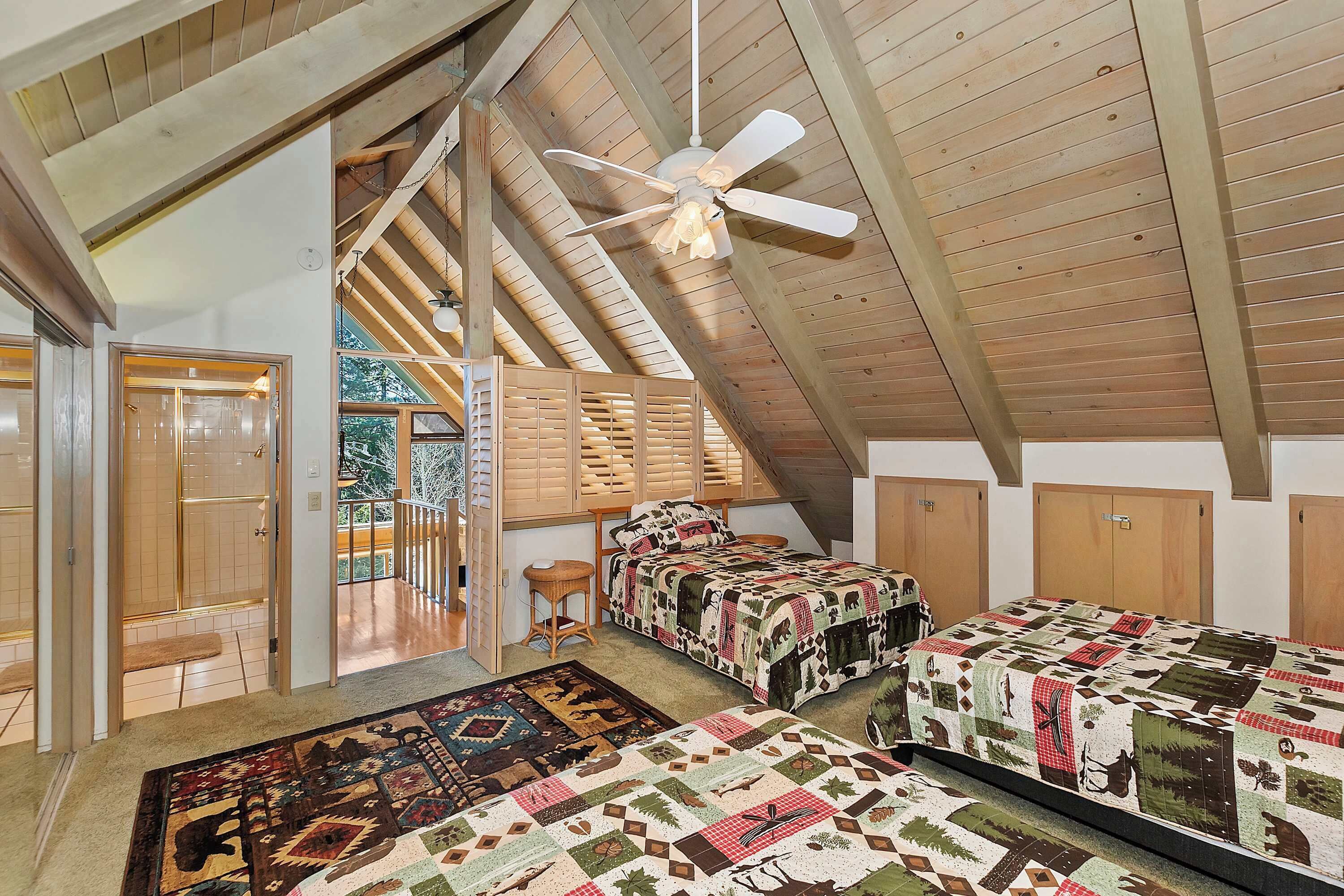 A high-ceilinged room with wooden beams, two beds with patterned quilts, a ceiling fan, and a view of the outdoors.