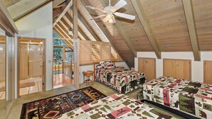 A high-ceilinged room with wooden beams, two beds with patterned quilts, a ceiling fan, and a view of the outdoors. - Bow N Arrow Lodge For 8! (Lake Arrowhead)