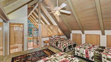 Una habitación con techos altos y vigas de madera, dos camas con colchas estampadas, un ventilador de techo y vistas al exterior.