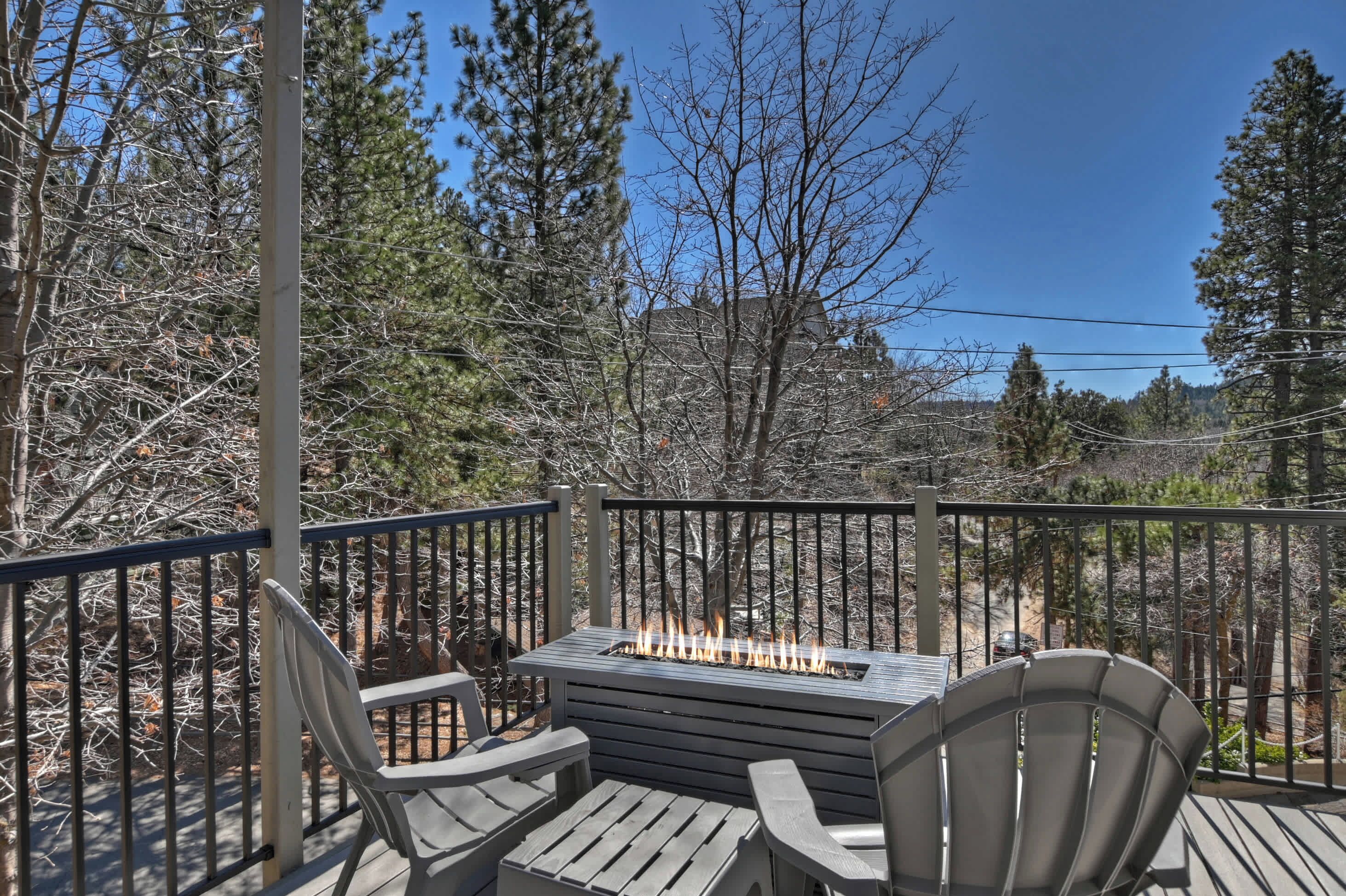 A deck with a fire feature, metal railings, and wooden chairs.