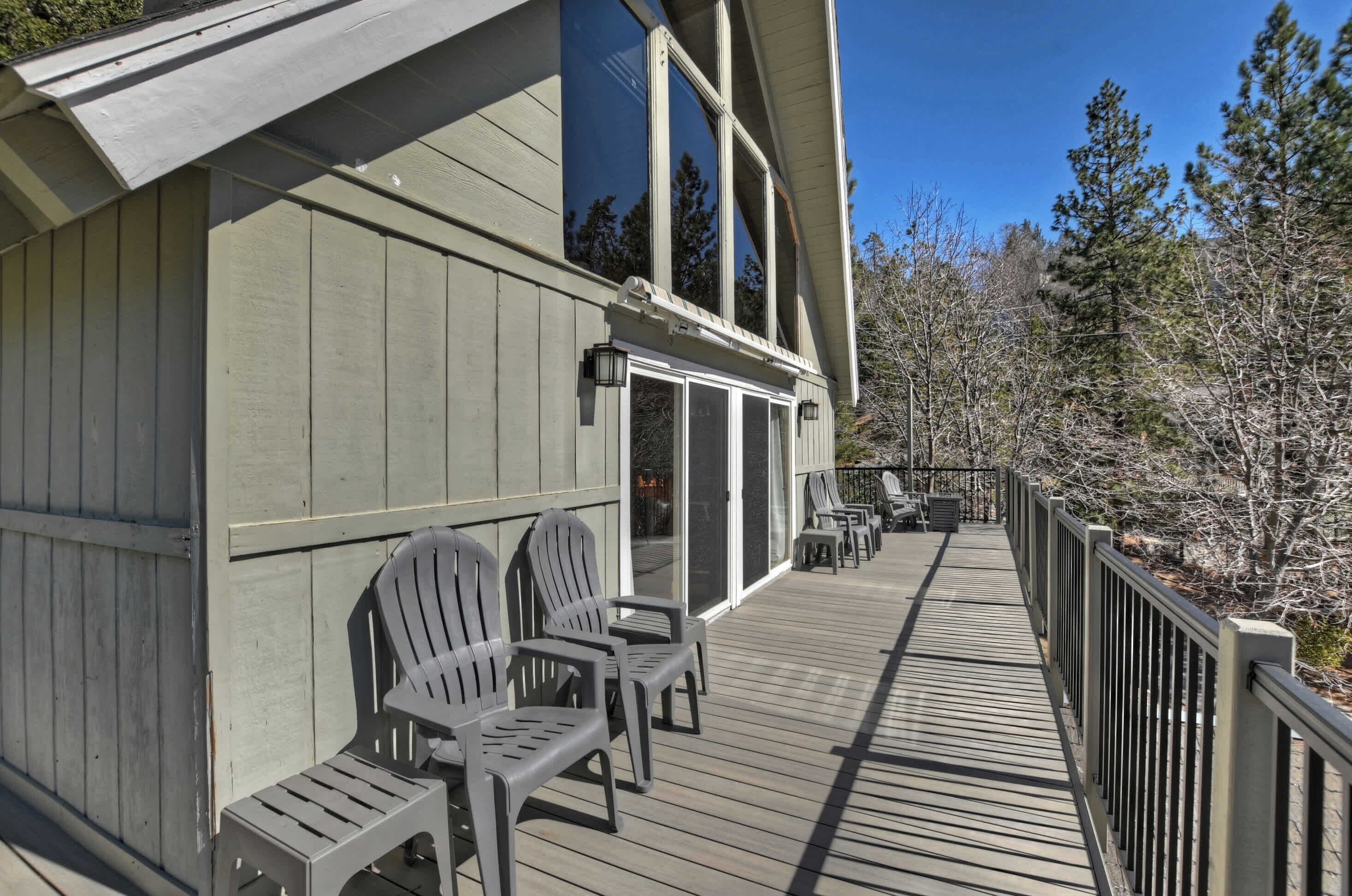 A wooden deck with Adirondack chairs, a railing, and a building with large windows and a sloped roof.